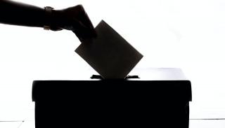 A silhouette of a hand placing a ballot slip into a ballot box