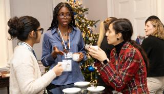 Three women talking around a table with a Christmas tree in the background