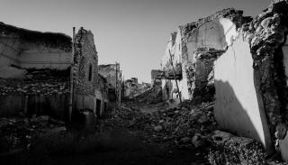 a black and white image of a street with the buildings destroyed through warfare therefore crumbling and falling apart 
