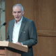 Roland Bleiker at a lectern in a grey suit with a white shirt delivering a keynote speech